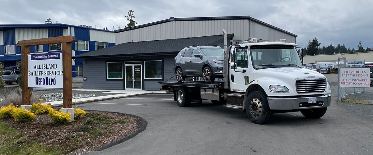 AIB tow truck with repossessed car on the back, at the Parksville office